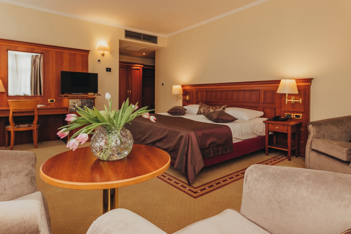 Une chambre d’hôtel avec un lit, un bureau, une télévision et un vase rempli de fleurs.