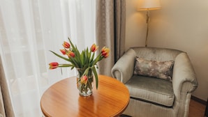 Une pièce avec une table ronde en bois, un fauteuil à rayures, un coussin à motifs floraux et une lampe.