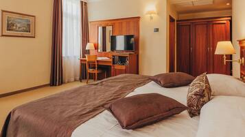 Una habitación de hotel con una cama grande, un escritorio con silla, un televisor y un armario.