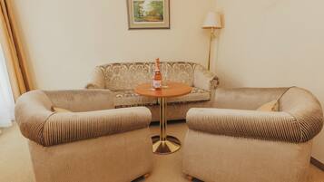 A room with a beige sofa, two armchairs, a small round table, a bottle of wine, and a framed picture on the wall.