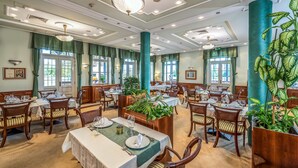 Un vaste espace dédié à la salle à manger, avec de nombreuses tables et chaises, de grandes fenêtres et des plantes décoratives.