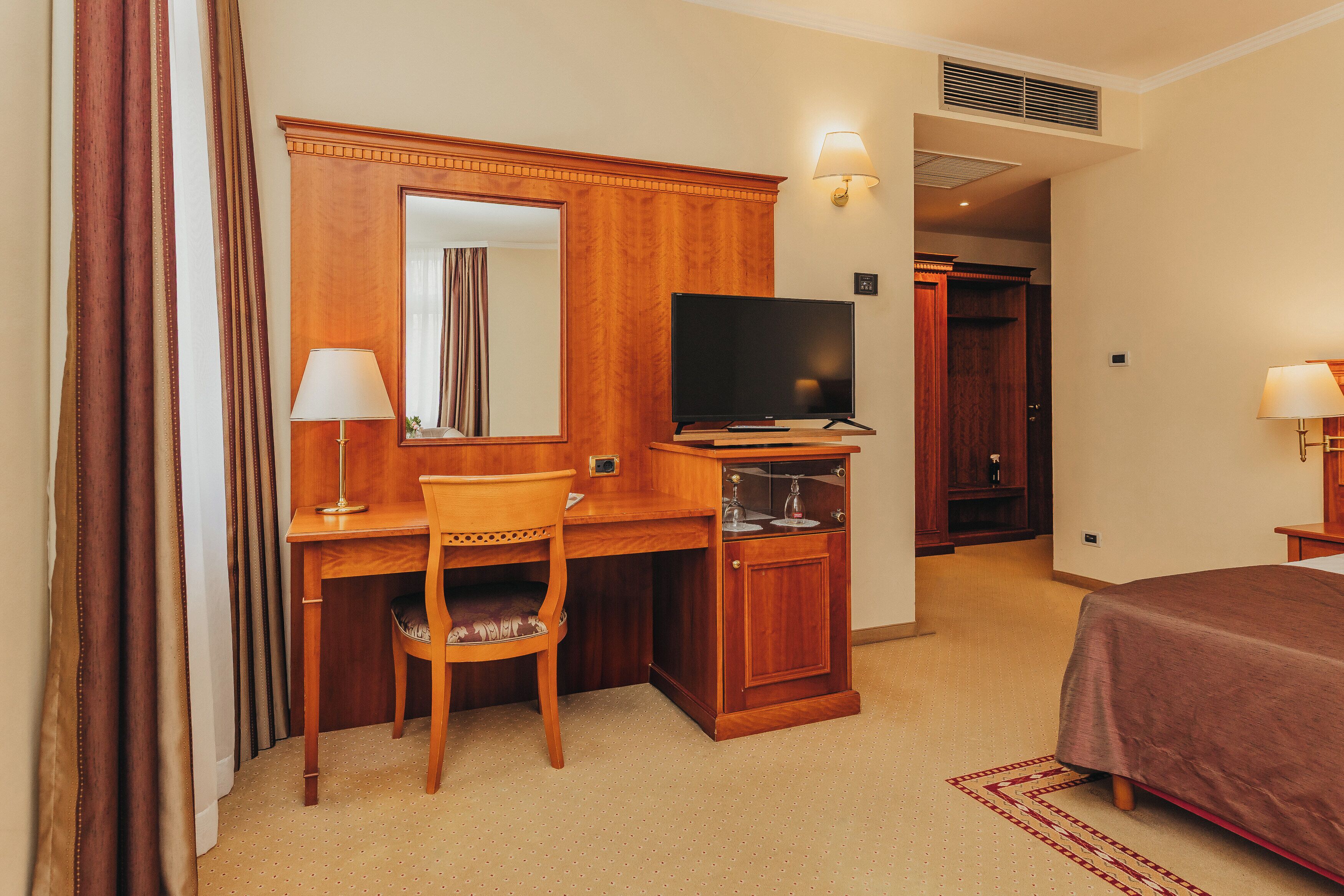 Une chambre d’hôtel avec un bureau en bois, une télévision, un lit et un miroir.
