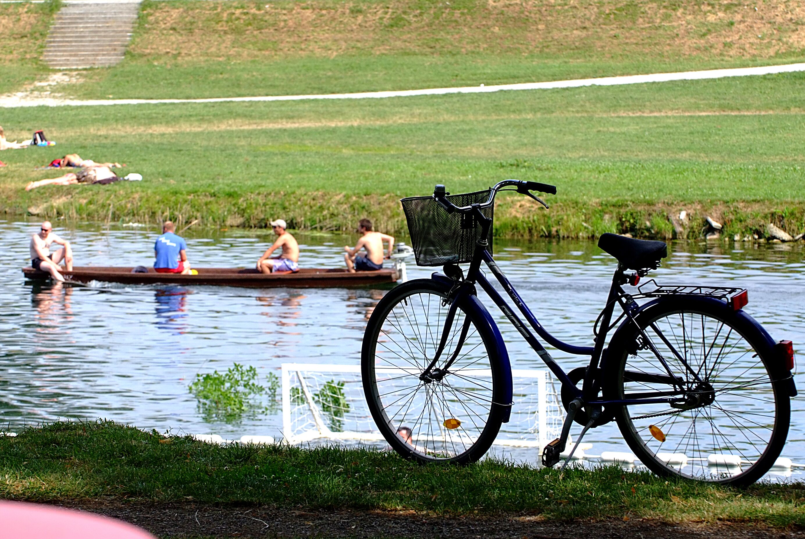 Una bicicleta amb un cistella aparcada vora un cos d'aigua tranquil·la.