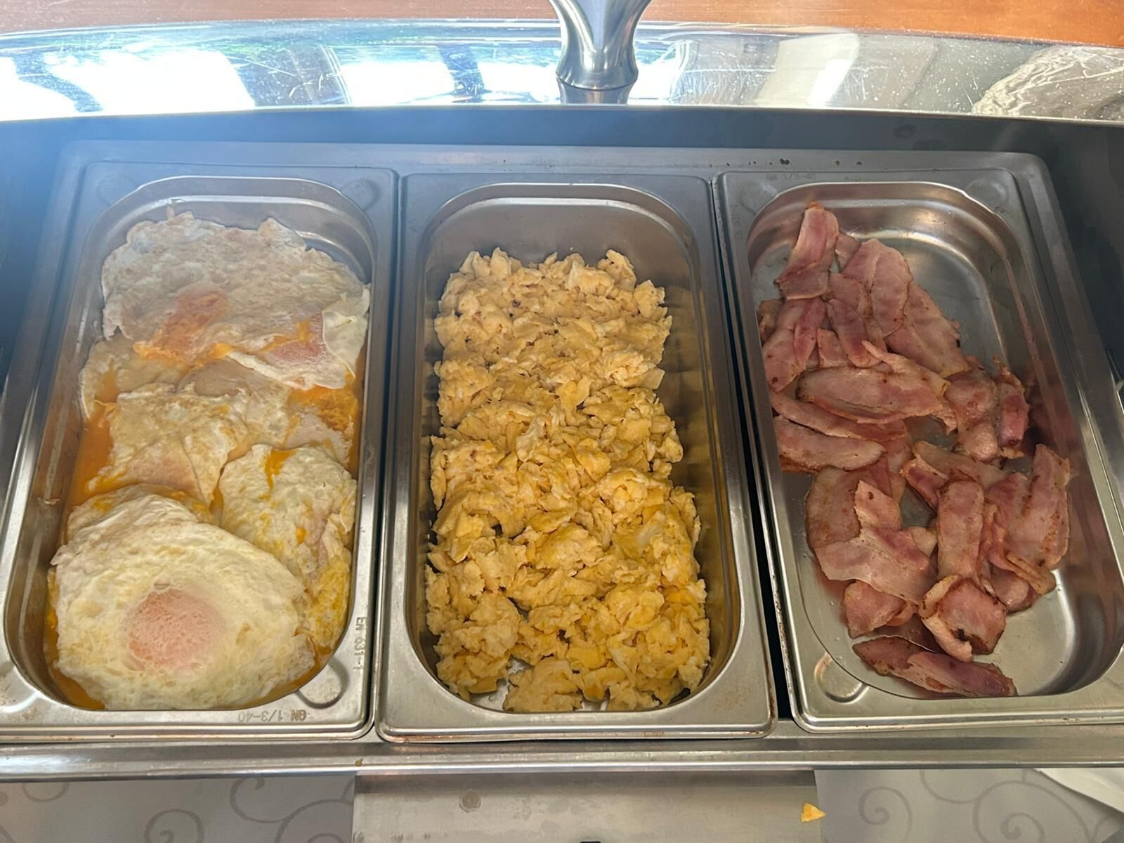 Un bufé con huevos revueltos, huevos fritos y tocino.