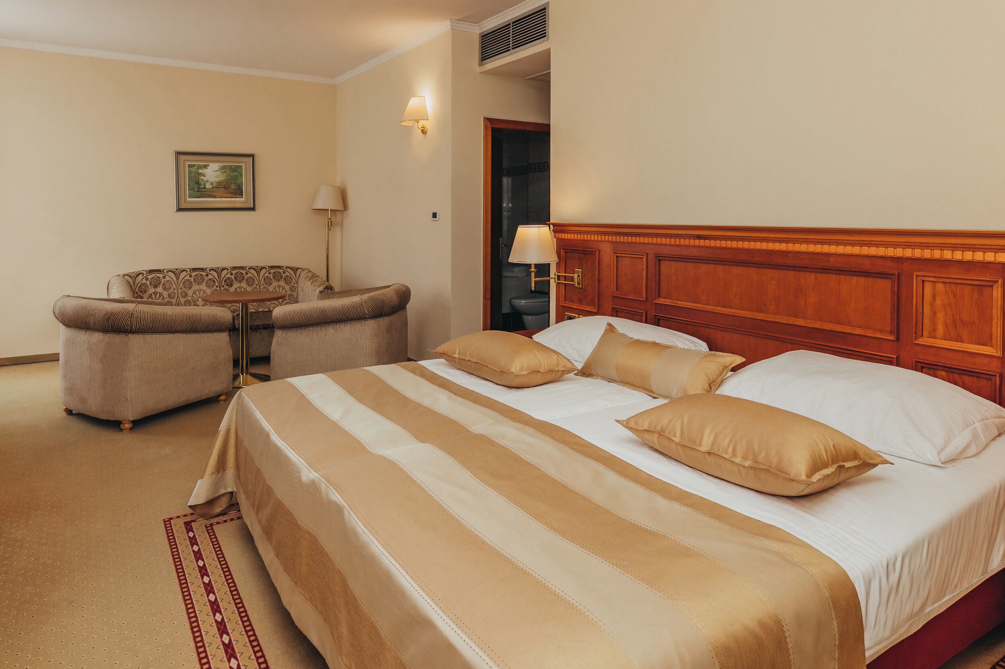 A hotel room with a large bed, a sofa, a small table, and a wall-mounted lamp.