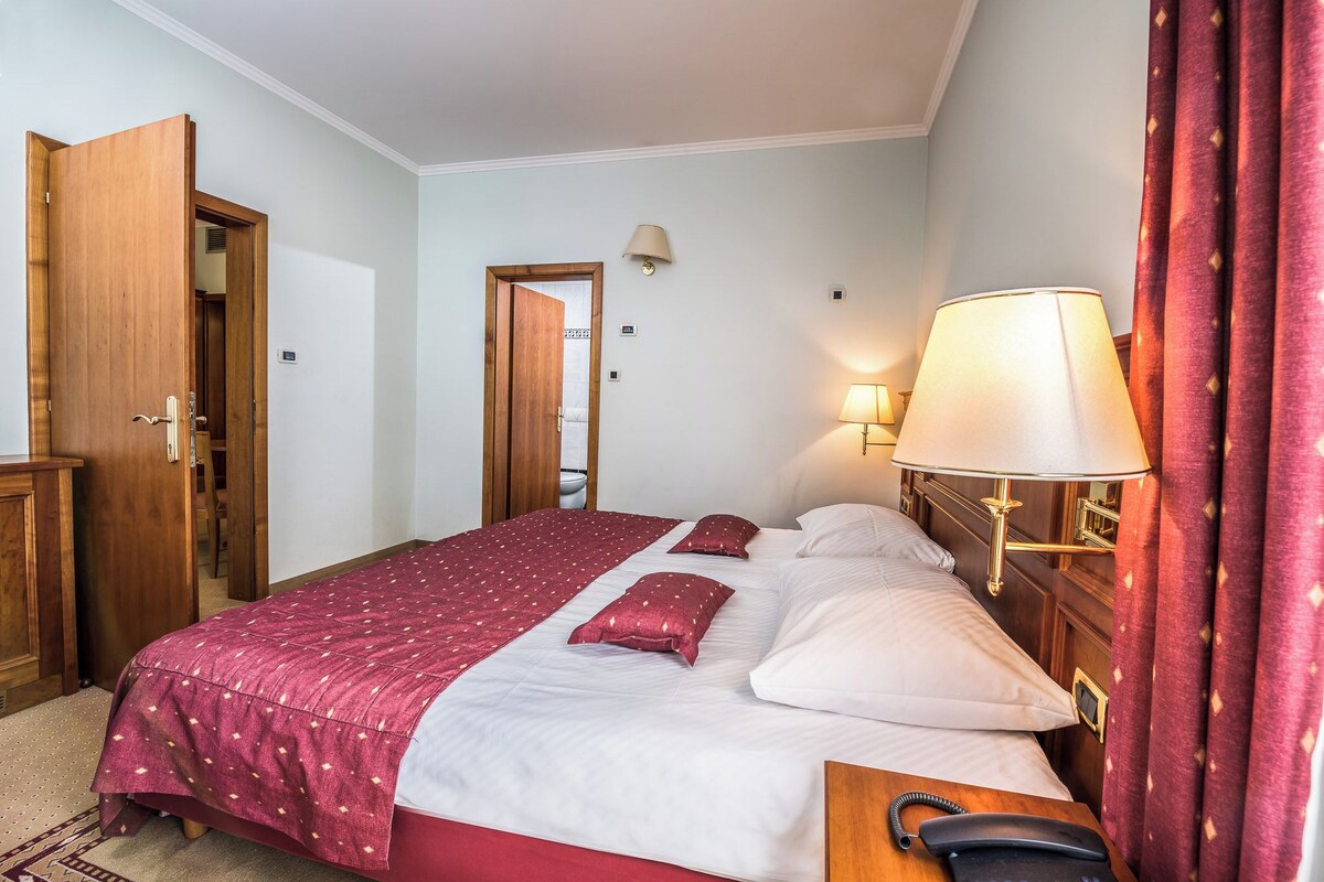Een hotelkamer met een bed, nachtkastje, lamp en garderobe.