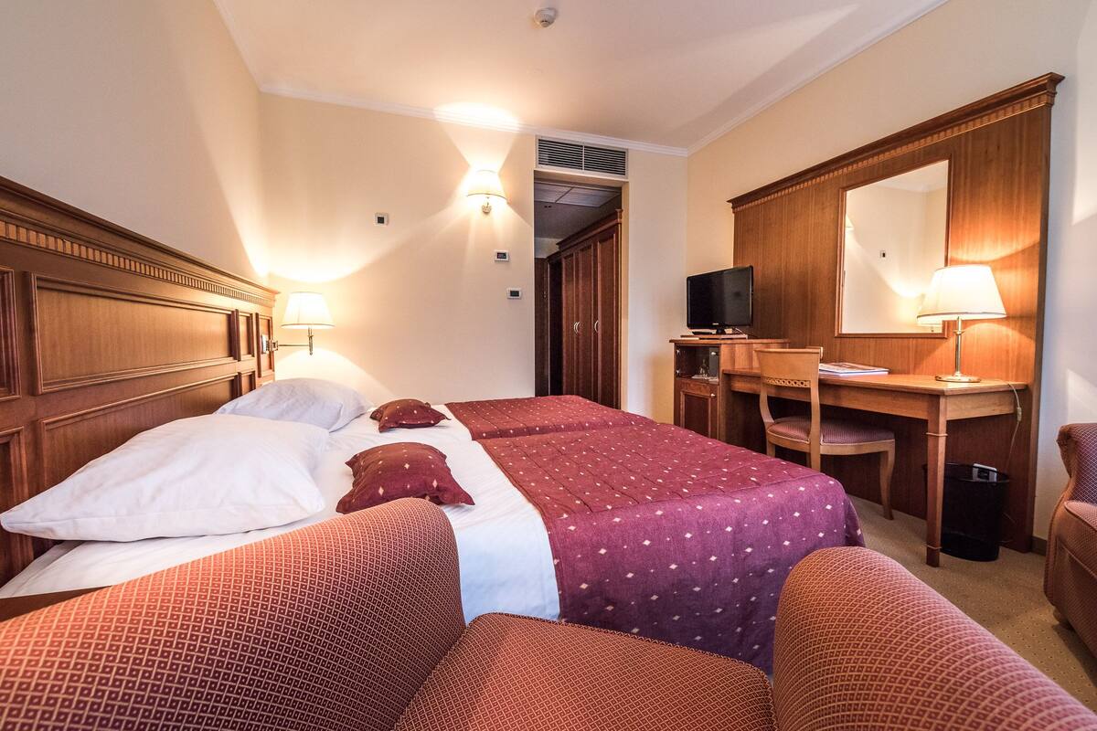 Een hotelkamer met een groot bed, twee nachtkastjes met lampen, een bureau met stoel en een grote spiegel.