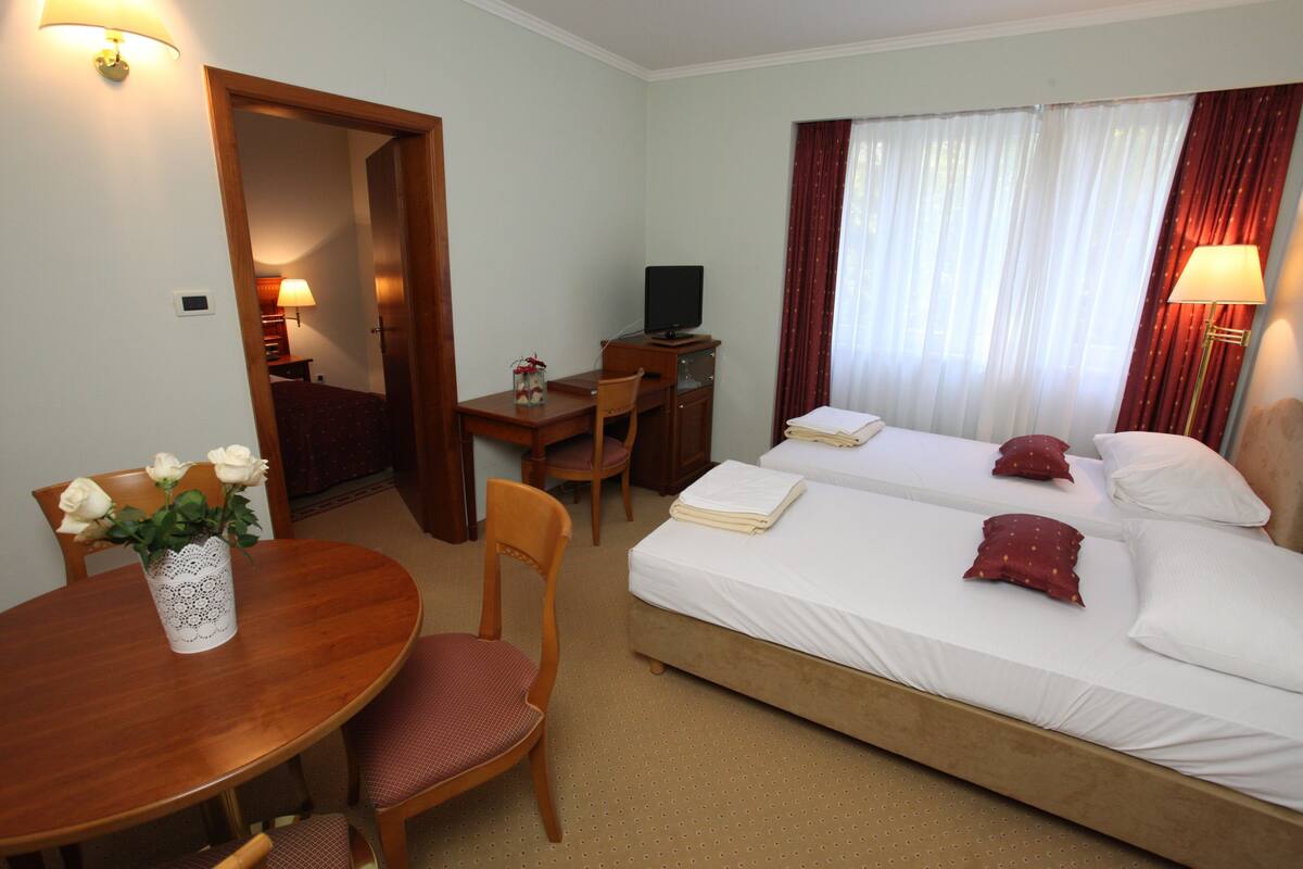 Hotelkamer met een bed, bureau met een computer, stoel, tafel met een bloevas en een lamp.