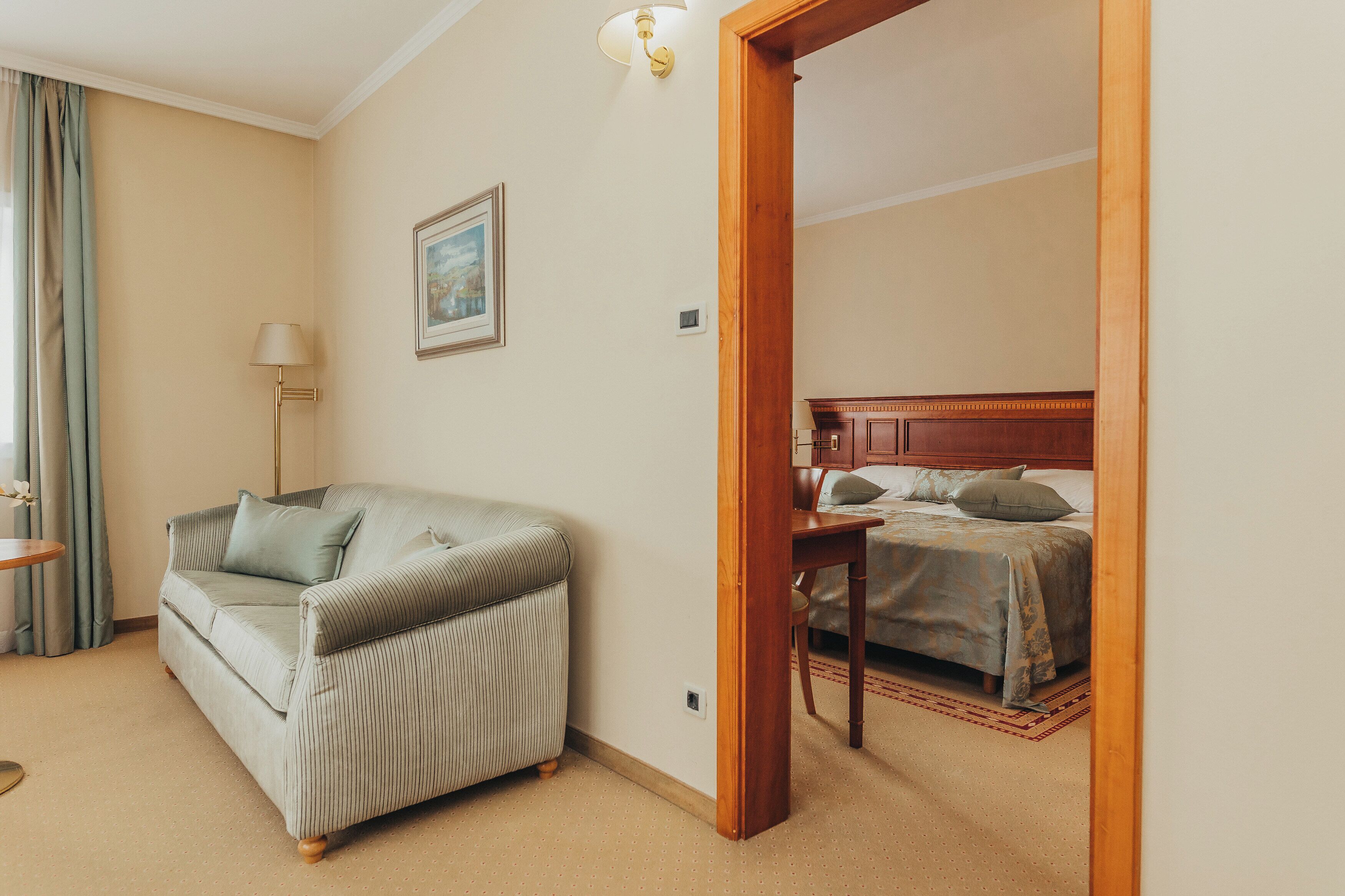 Ein Hotelzimmer mit einem gestreiften Sofa, einem Bett mit Holz Kopfteil, einem kleinen Tisch und einem Bild an der Wand.