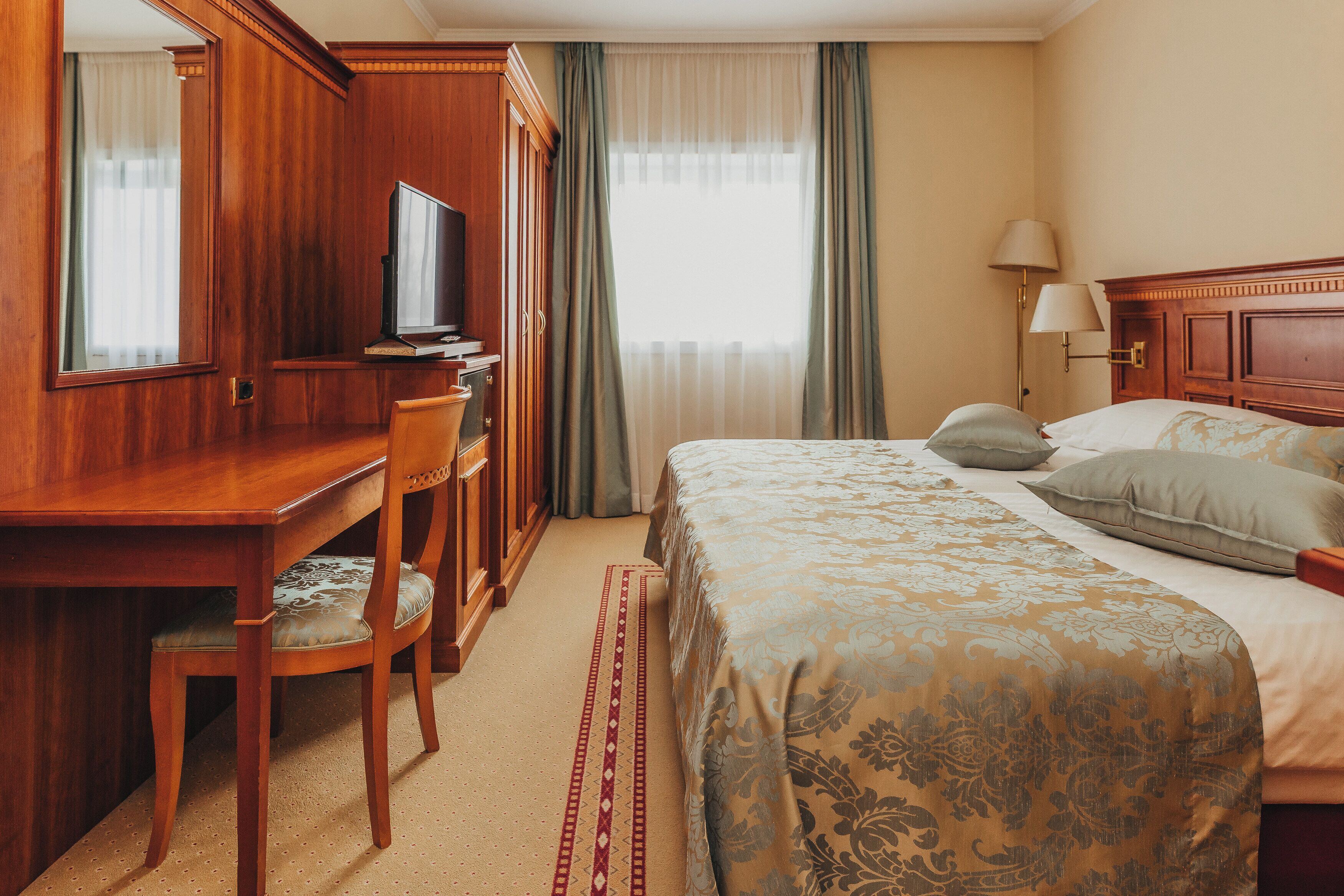 A hotel room with a wooden desk, television, and a bed with patterned bedding.