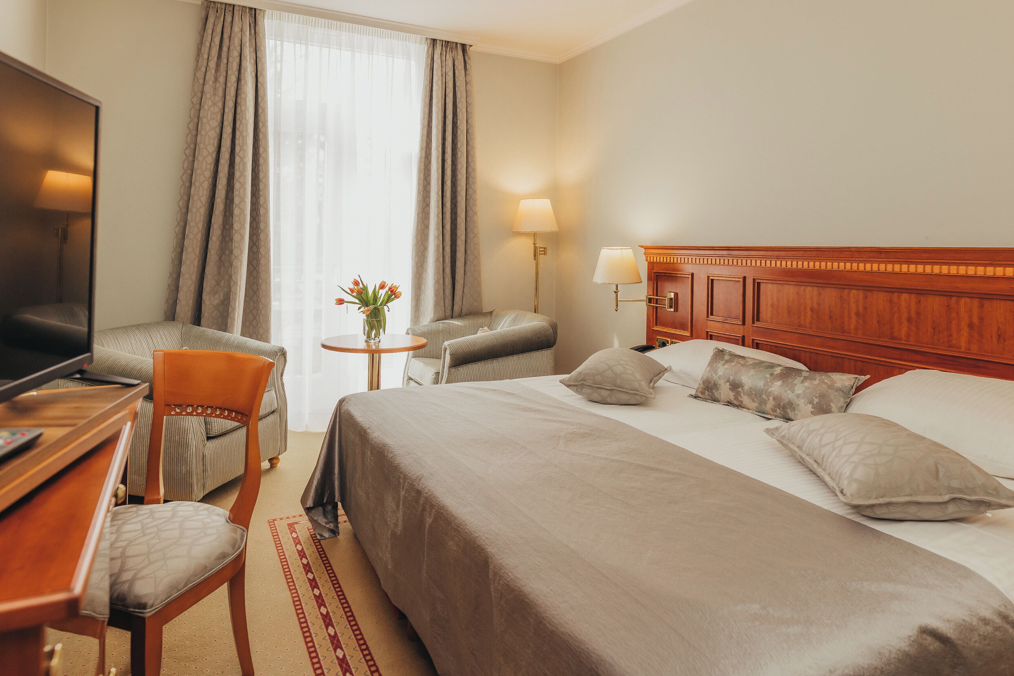Habitació d'hotel amb llit, escriptori amb televisió, cadira, taula petita amb un ram de flors i làmpada.