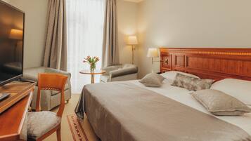 Habitació d'hotel amb llit, escriptori amb televisió, cadira, taula petita amb un ram de flors i làmpada.