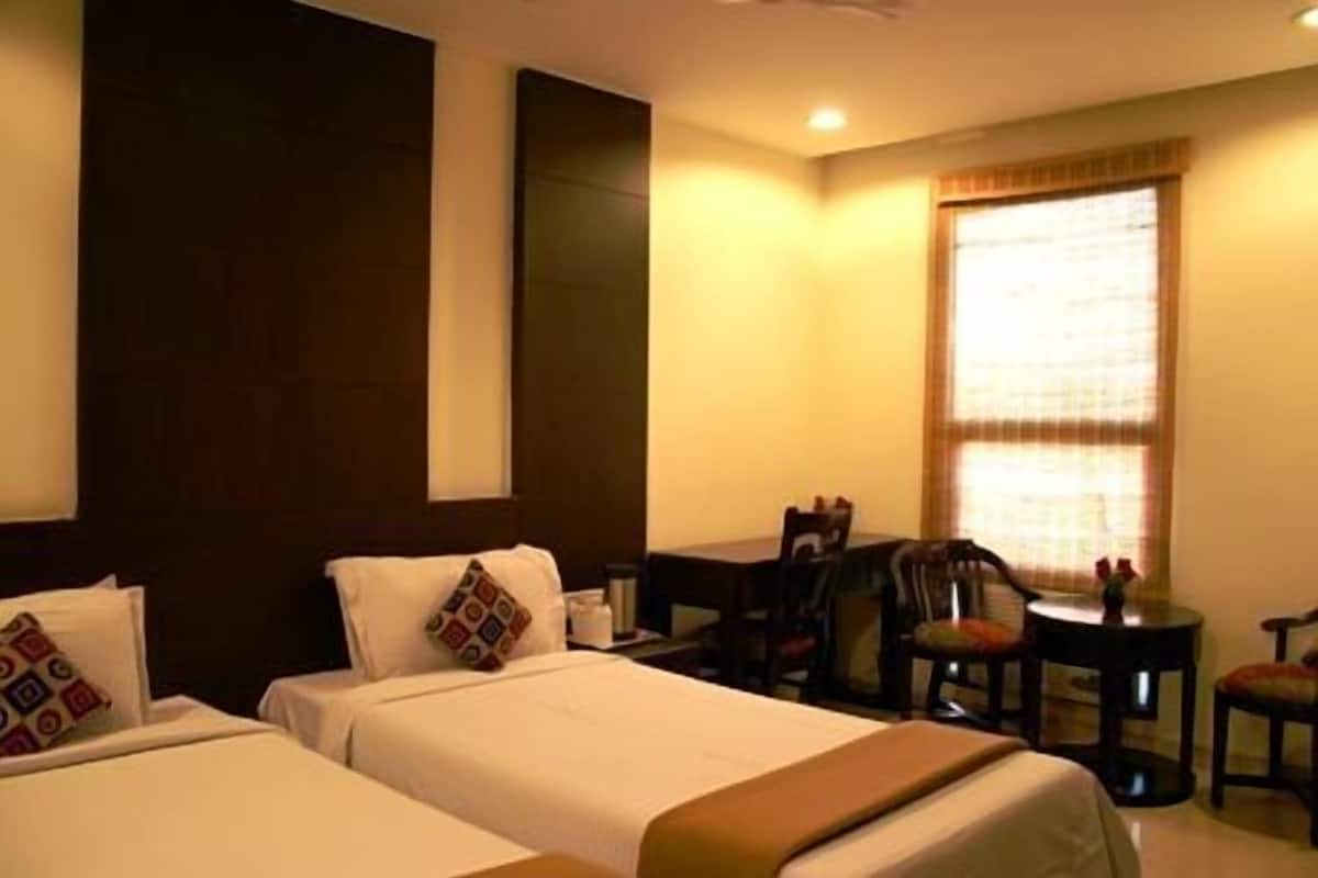A hotel room with two beds, a desk, a chair, and a small table.