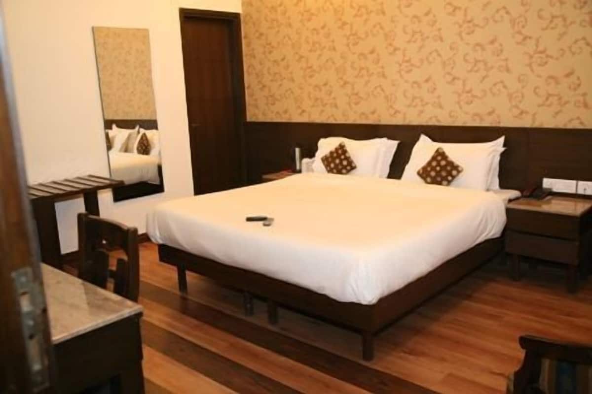 A neatly made bed with white linens and brown pillows, a wooden nightstand with a lamp, and a mirror on the wall.