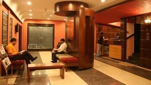 A lobby with a reception desk, seating area, and a large window with blinds. - Hotel Grand Peepal (New Delhi)