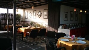 An outdoor dining area with tables and chairs, a wooden ceiling, and framed pictures on the walls. - Hotel Grand Peepal (New Delhi)