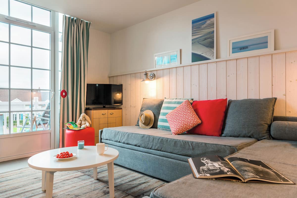 A modern living room with a sofa, a small table with a plate of fruit, a TV, and a window with curtains.