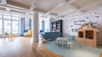 A spacious room with a wooden floor, a blue sofa, yellow chairs, a bookshelf, and a wooden playhouse.