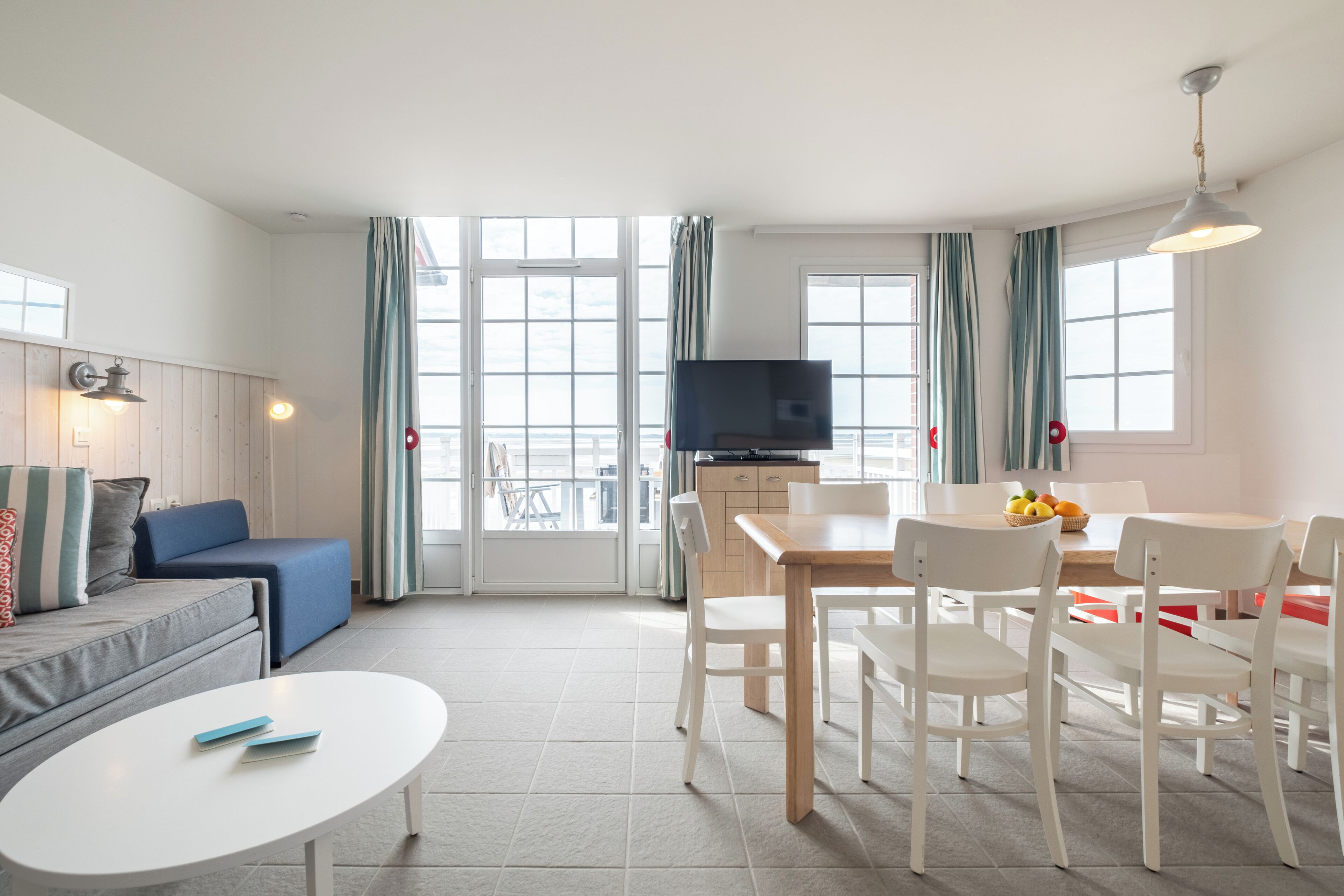 Een moderne woonkamer met een bank, een eettafel met stoelen, een televisie en een keukenhoek.
