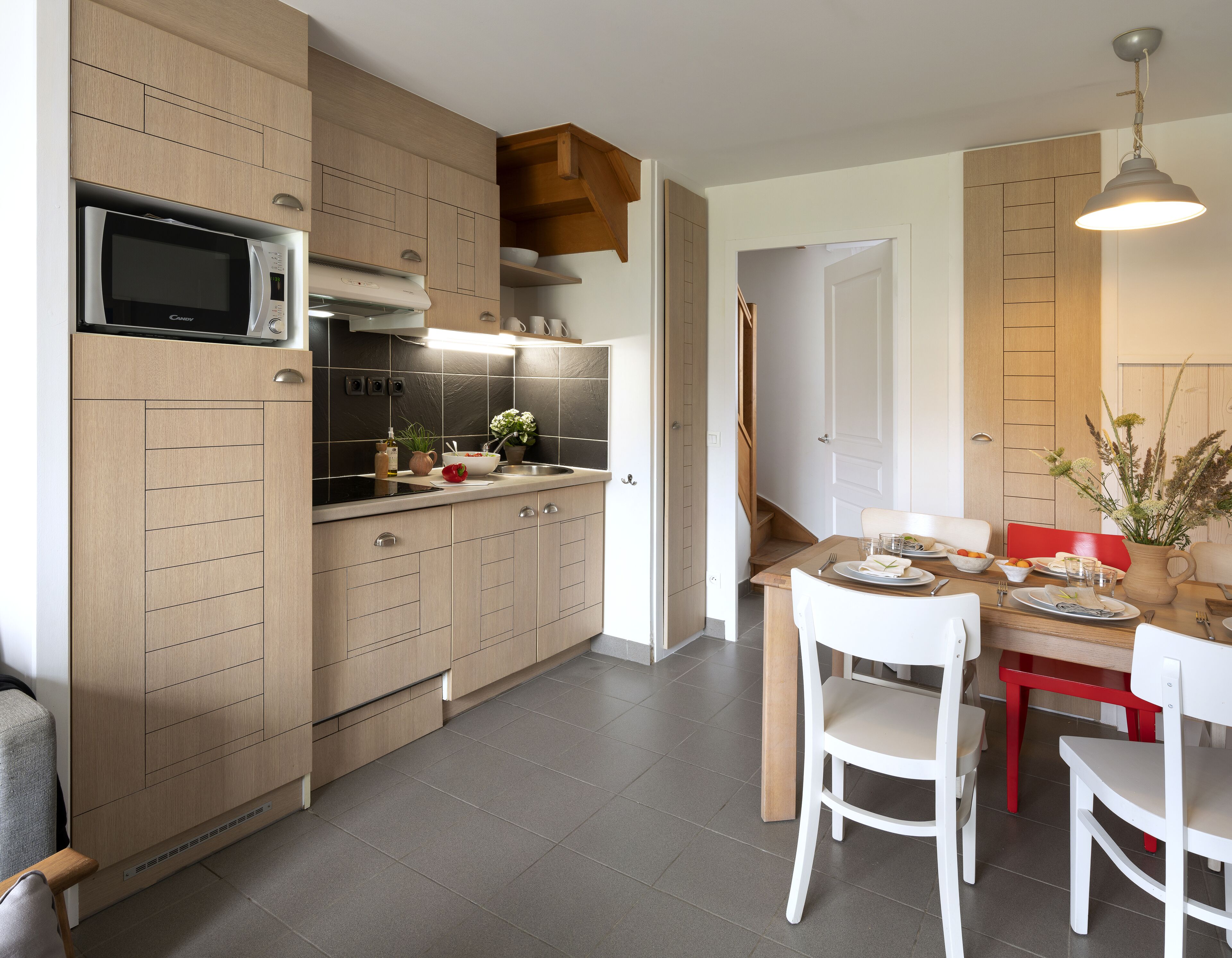 A modern kitchen with wooden cabinets, a microwave, and a dining area with a table and chairs.