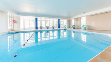 An indoor swimming pool with clear blue water, a starting block, and several empty buckets on the poolside.
