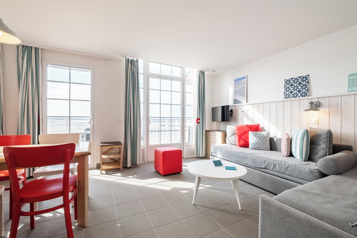 A modern living room with a grey sofa, red chair, and a small white table.