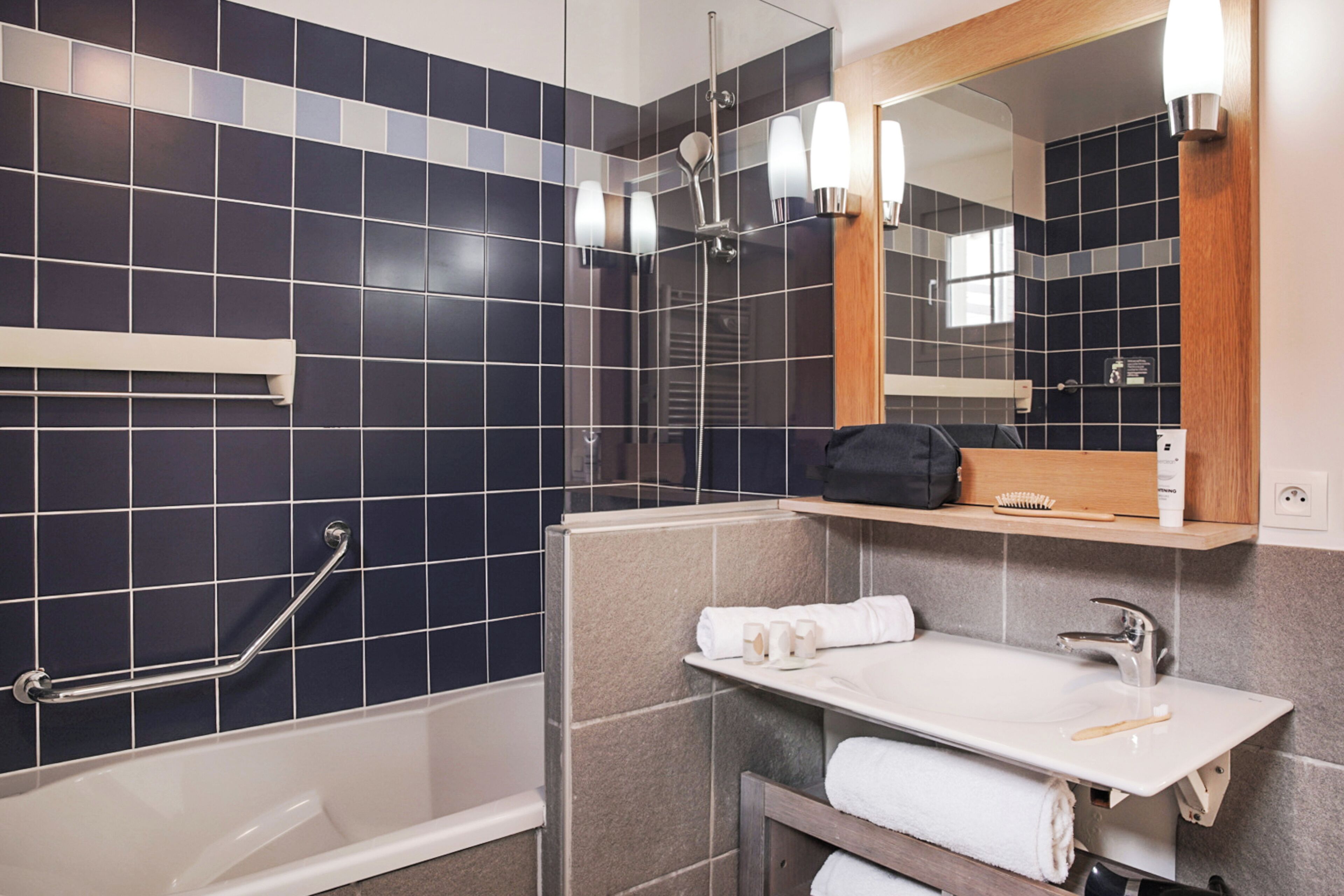 A modern bathroom with a bathtub, shower, and sink. There is a mirror above the sink and a towel rack.