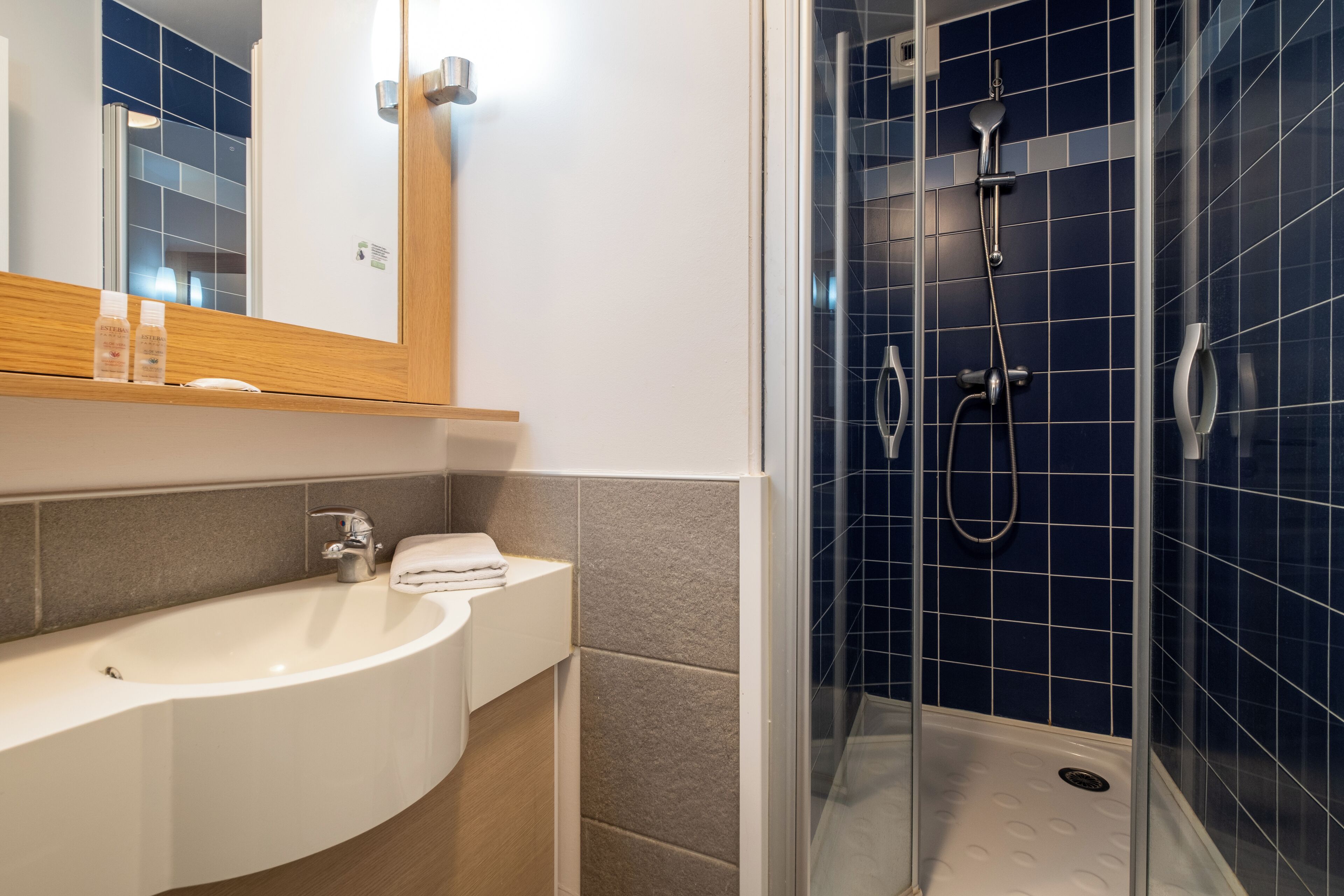 Une salle de bain moderne avec un lavabo blanc, un miroir et une douche vitrée, le tout agrémenté de carreaux bleus.