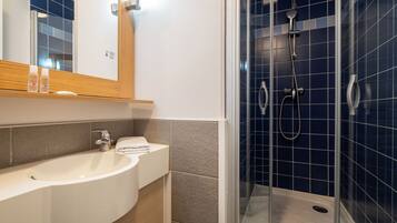 Une salle de bain moderne avec un lavabo blanc, un miroir et une douche vitrée, le tout agrémenté de carreaux bleus.
