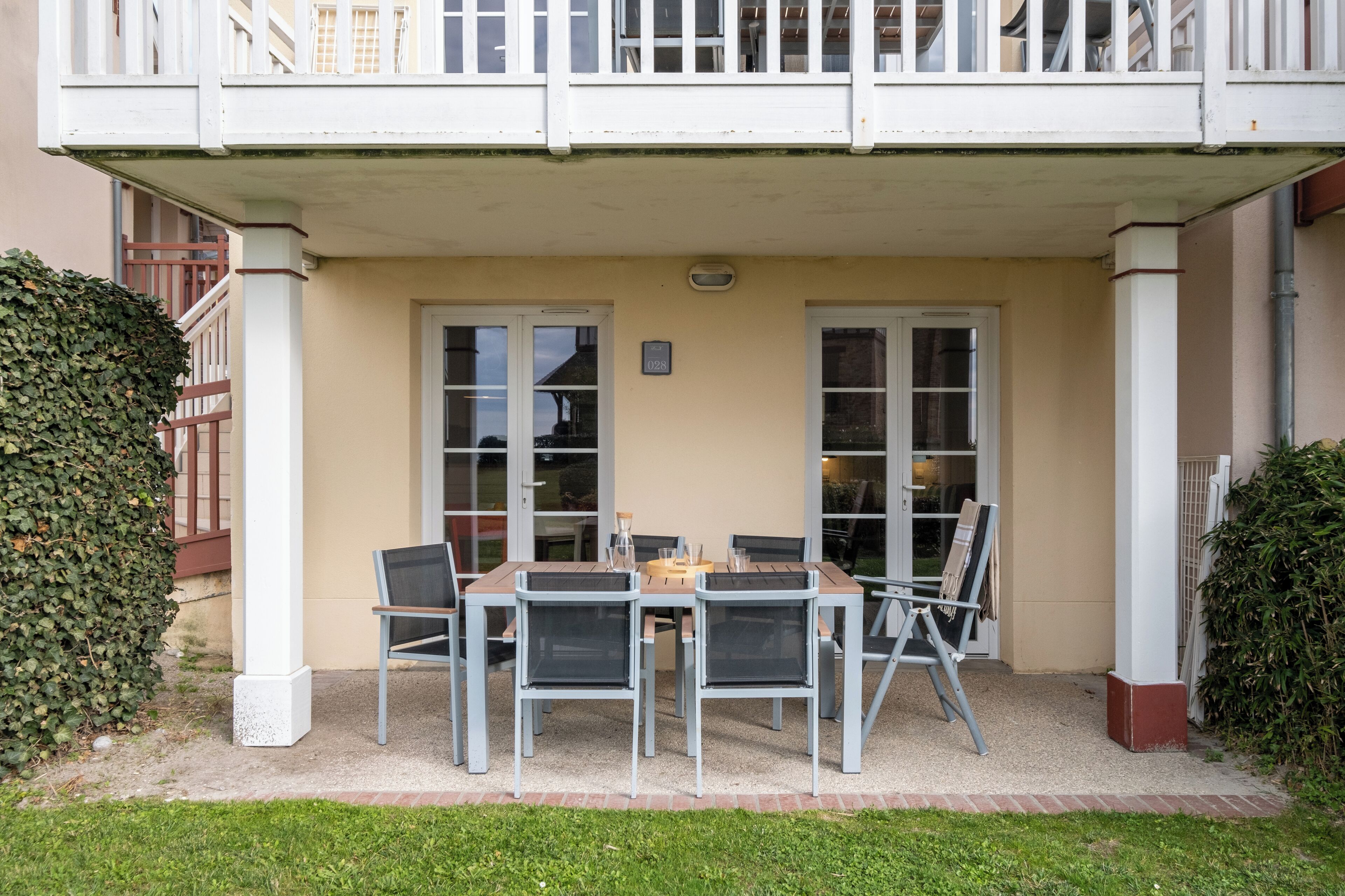 Un espace extérieur abrité avec une table et des chaises, une petite table avec un verre, et une enseigne au-dessus de la porte.