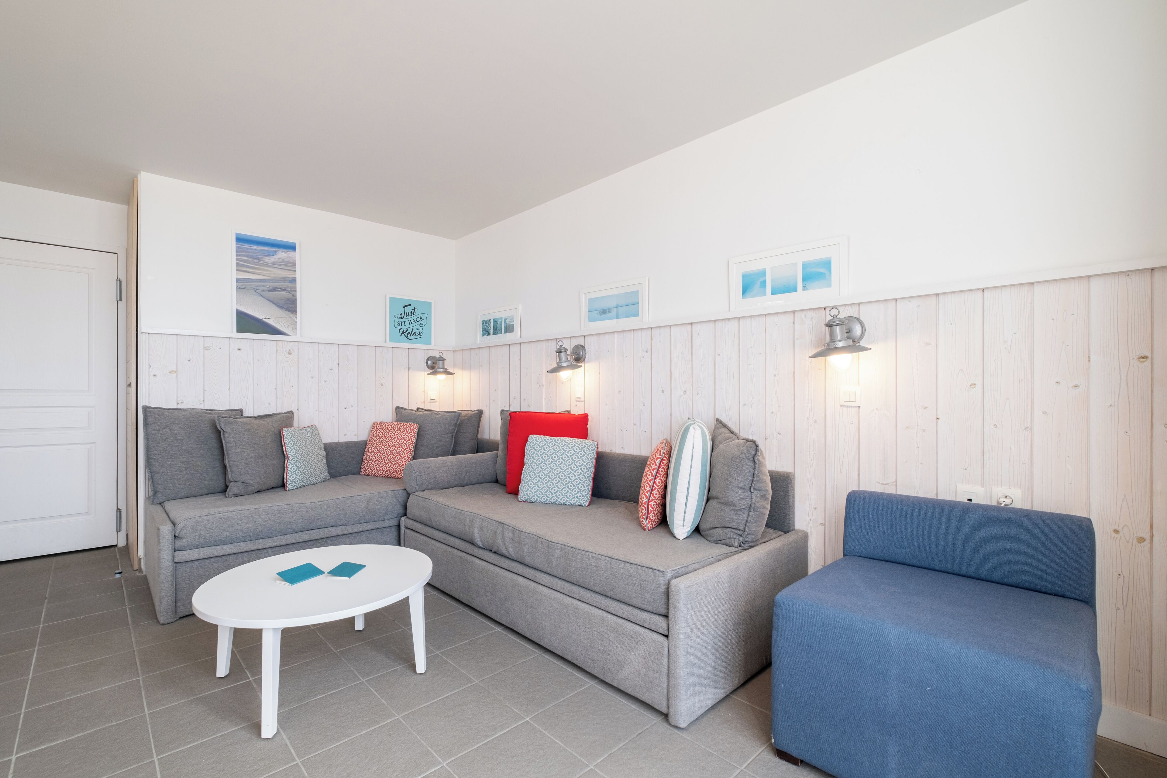 Una sala de estar moderna con un sofá seccional gris, un sillón azul y una mesa de centro blanca. Hay luces empotradas en las paredes y cuadros enmarcados.