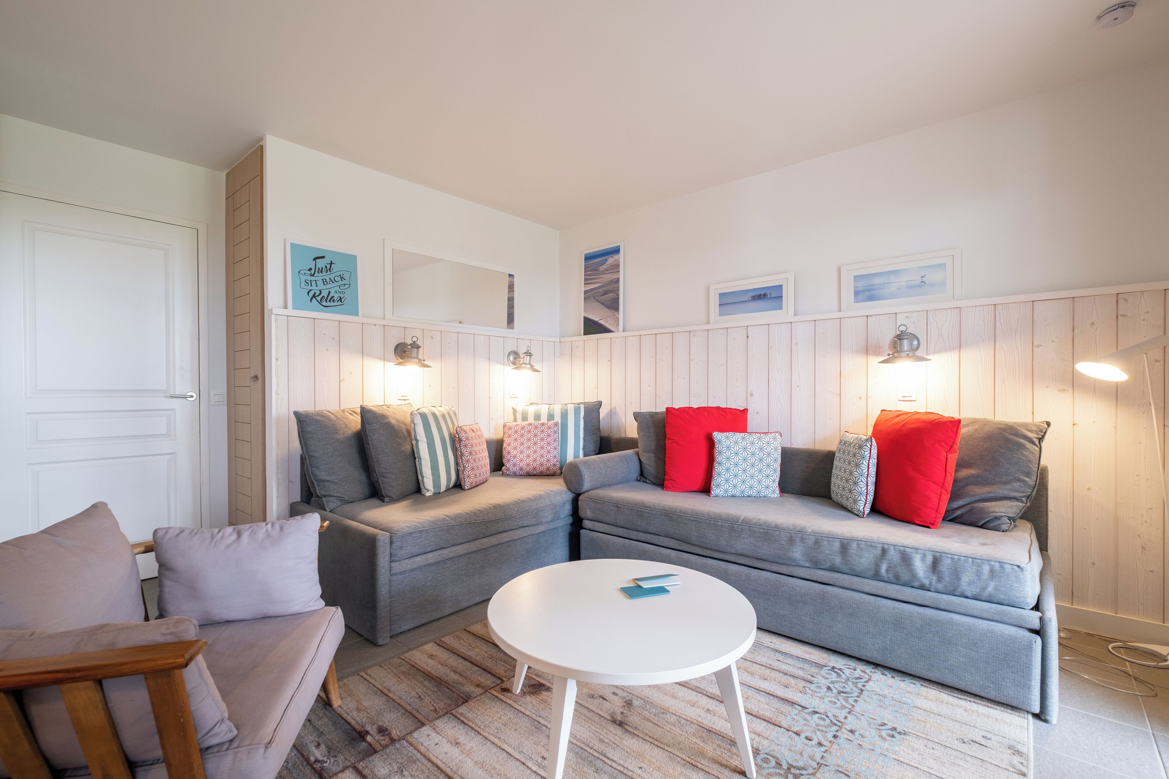 Een gezellige woonkamer met twee grijze banken, een houten stoel en een witte salontafel.