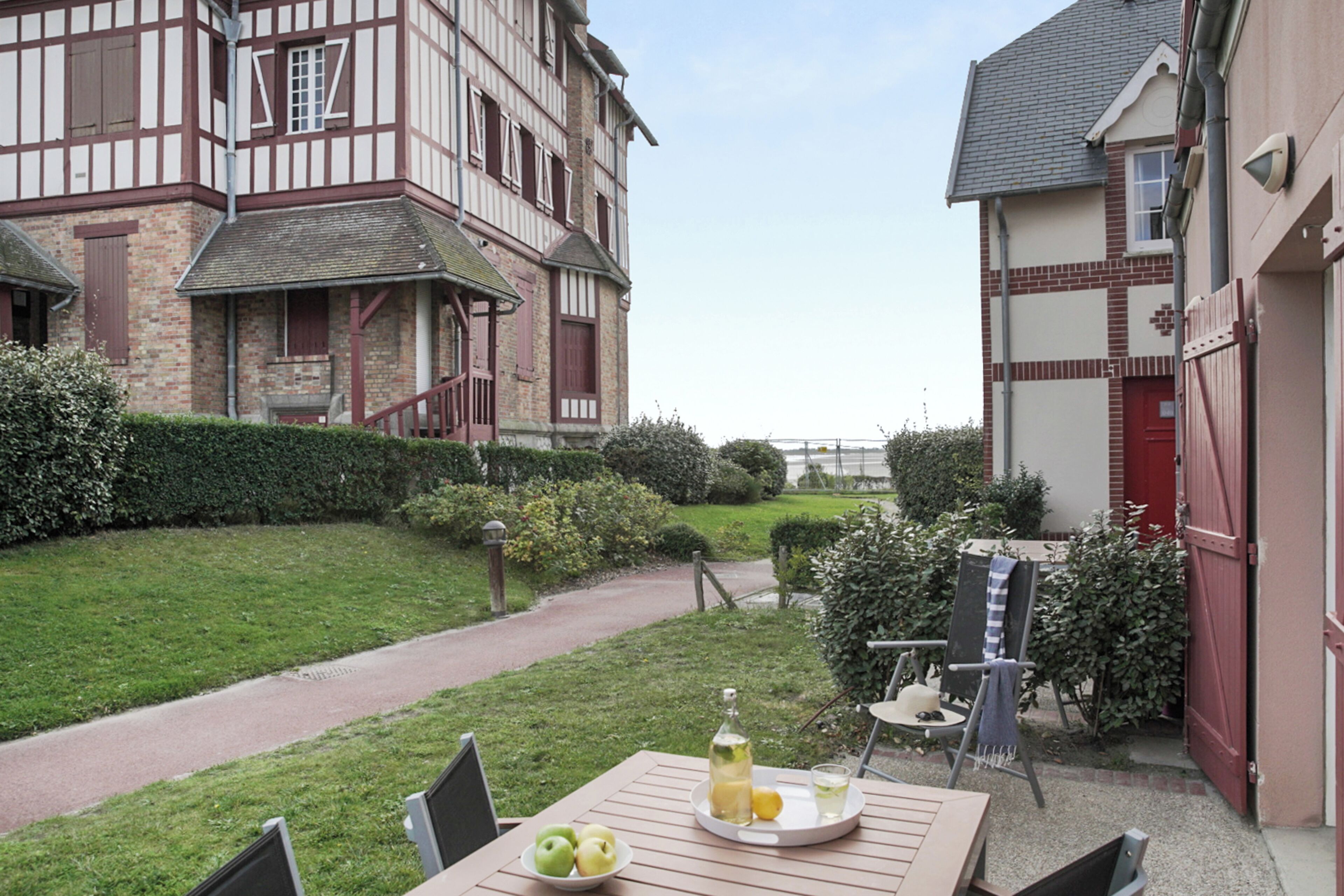 A courtyard with a wooden table, a chair, a bench, and a small garden area with a hedge and a path.