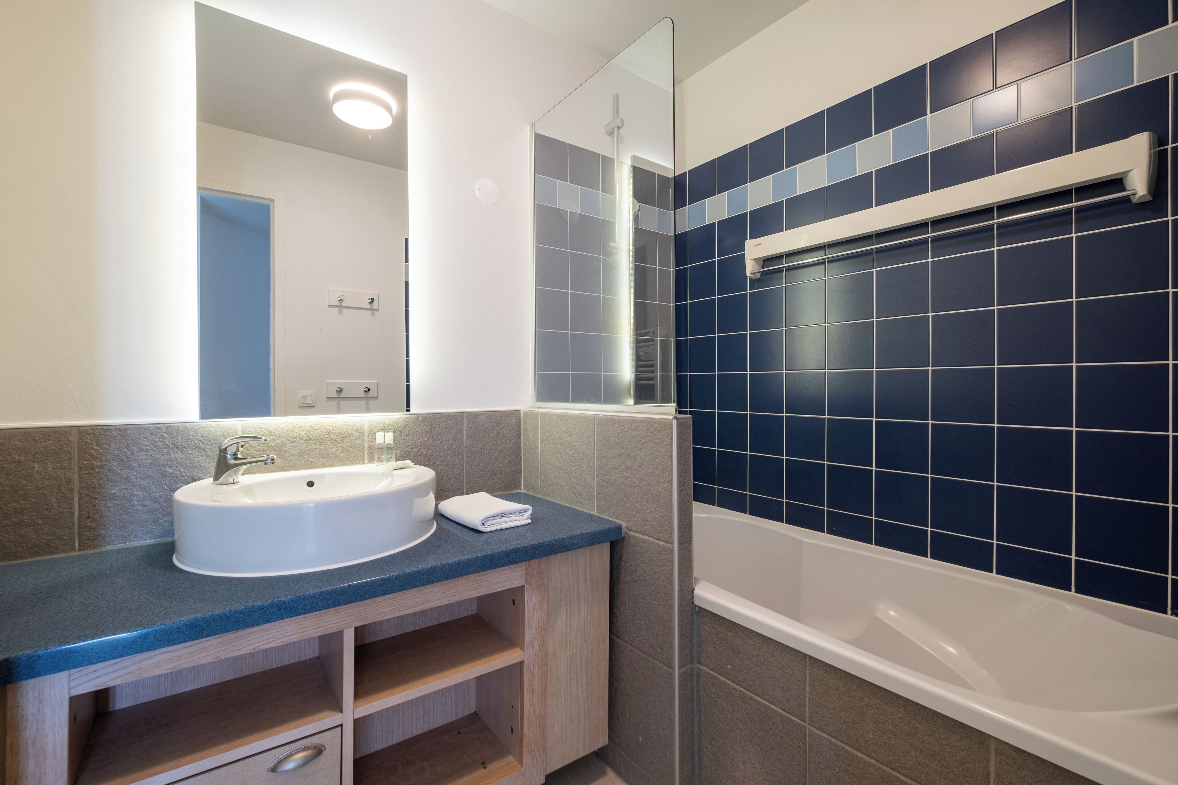 Un baño con lavamanos blanco, un espejo, ducha y paredes con azulejos azules.
