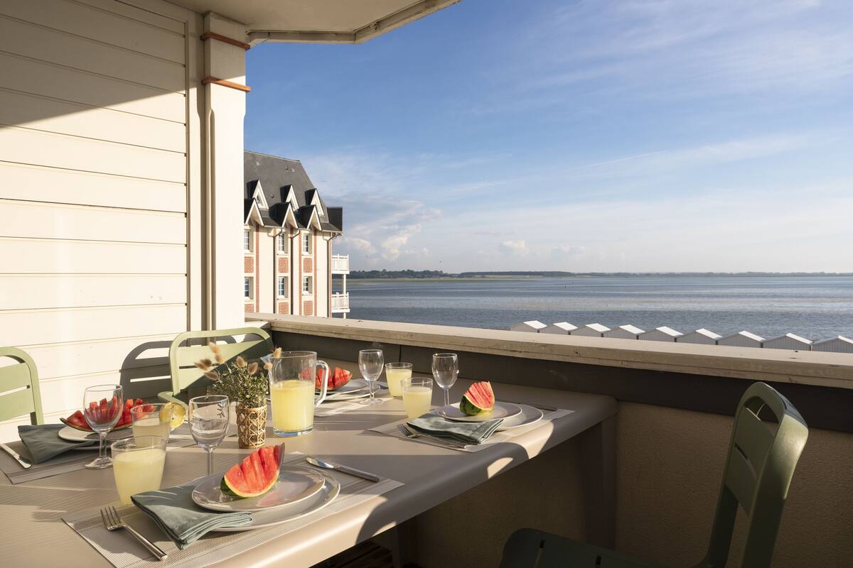 A table set for two with a view of the sea, a wicker basket, and a potted plant.