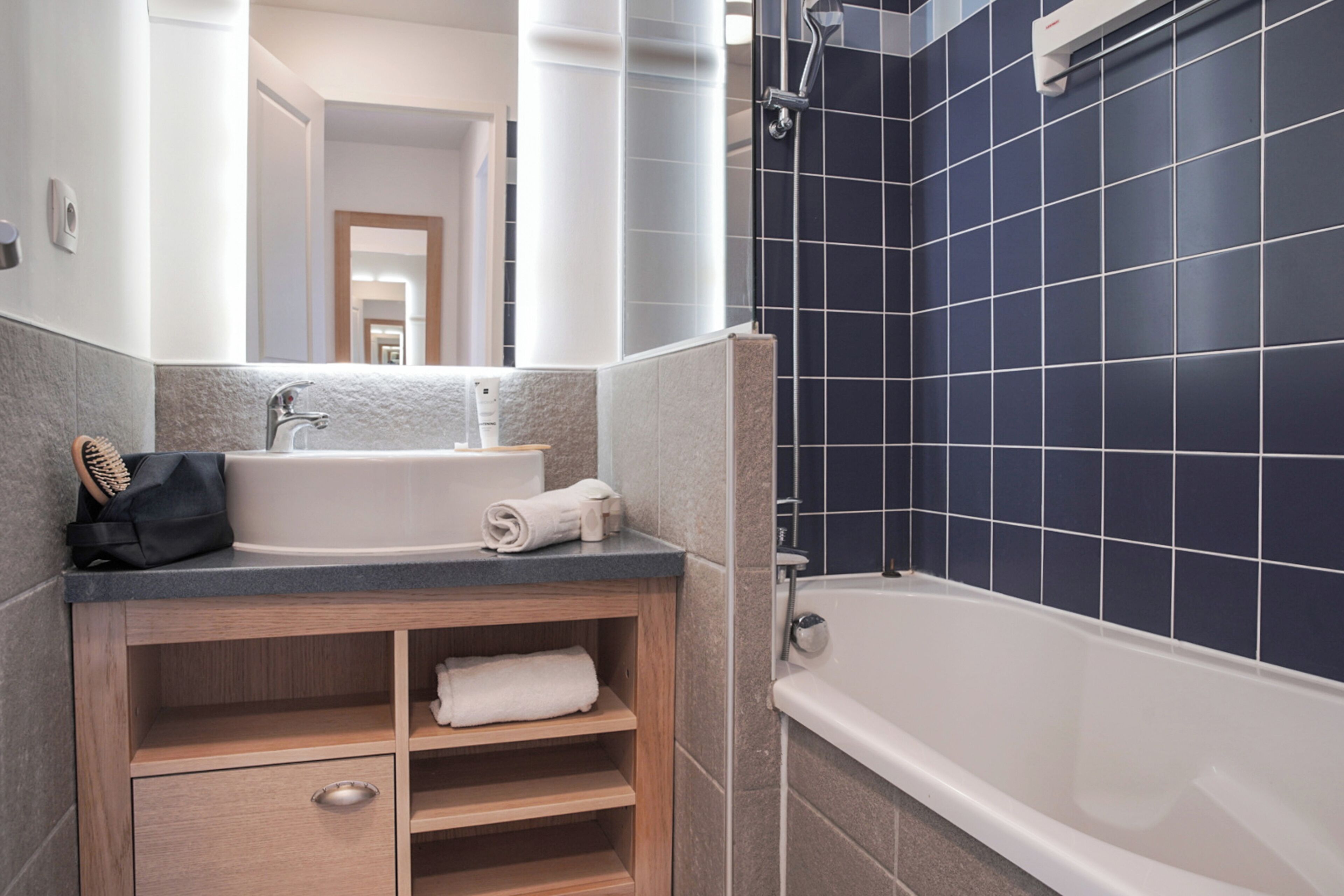 A modern bathroom with a bathtub, a sink, and a mirror. There are towels and toiletries on the counter.