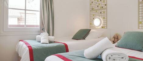 A hotel room with two beds, a window with curtains, a wall-mounted light, and a teddy bear on one bed.