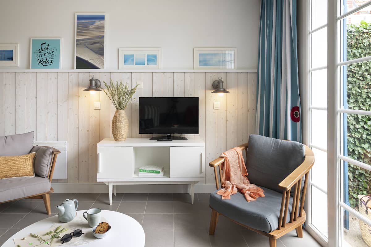 A living room with a TV, white cabinet, wooden chair, and a window with curtains.