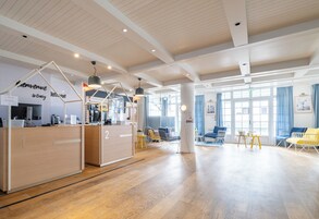 Un vestíbulo espacioso con suelo de madera, un mostrador de recepción, zona de estar y ventanas amplias que dejan entrar luz natural.