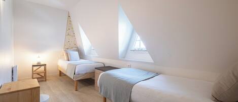A small, modern bedroom with two beds, a wooden cabinet, and a small table.