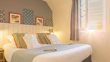 A neatly made bed with white linens and striped pillows, a bedside table with a lamp, and a window with curtains.