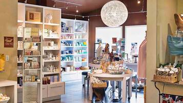 Una tienda boutique con estantes llenos de diversos productos, una mesa expositora central e iluminación colgante.