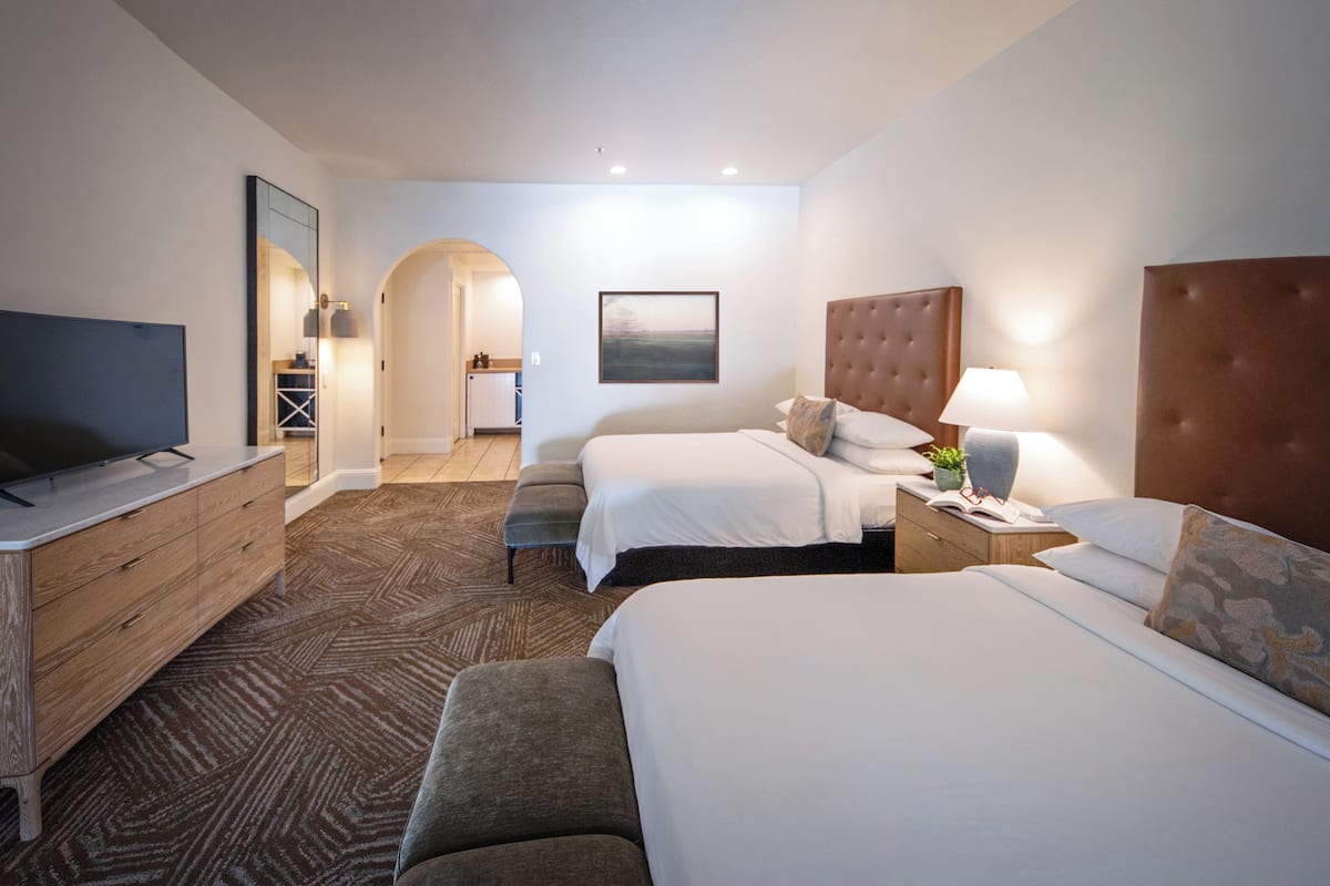 A hotel room with two beds, a TV, a wooden dresser, and a large mirror.