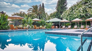 A swimming pool with lounge chairs and umbrellas, surrounded by greenery.