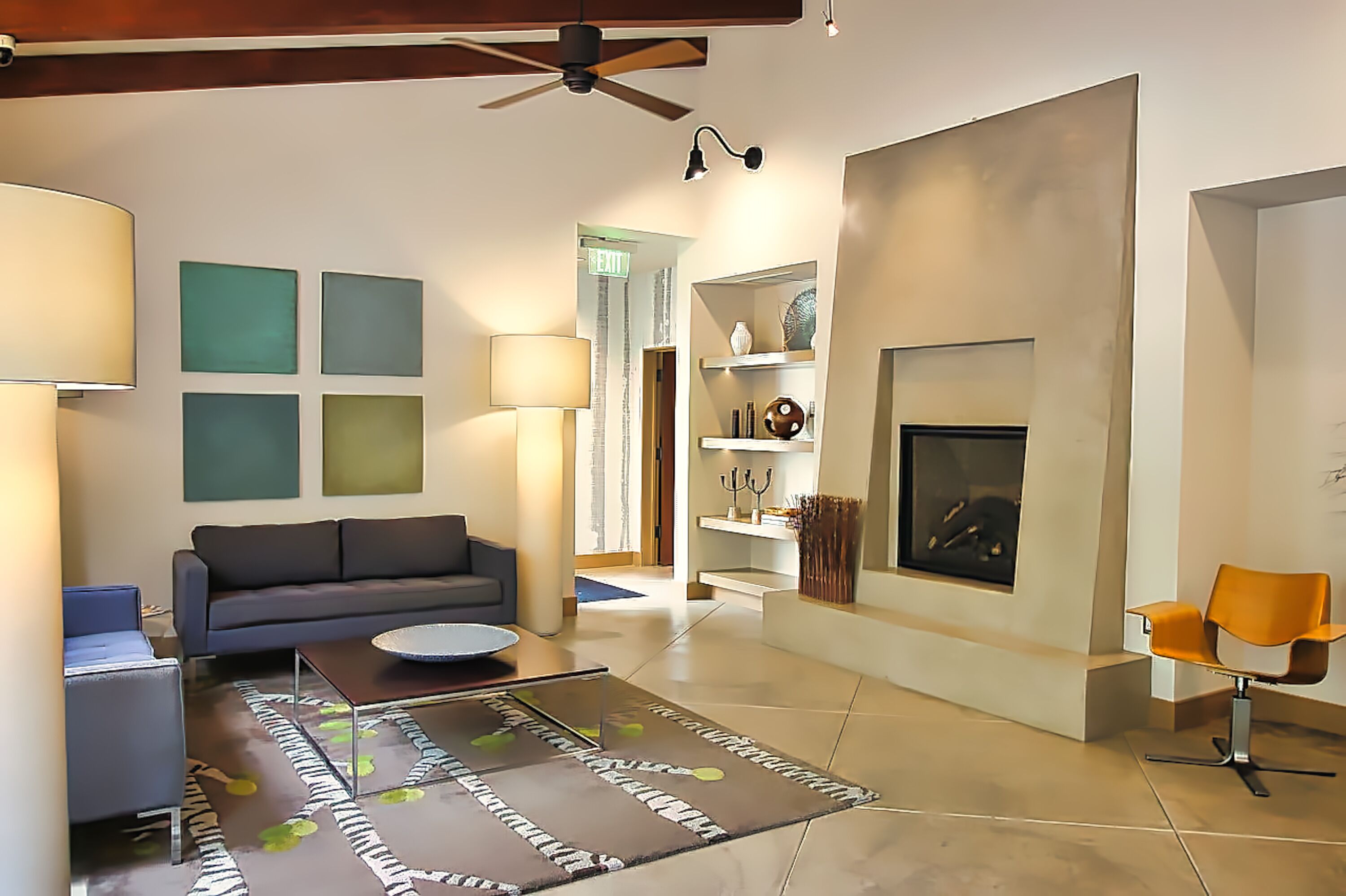 A modern living room with a sofa, coffee table, and orange chair. There is a fireplace and a ceiling fan.