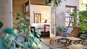 A room with a bed, a table with a lamp, and two wooden chairs.
