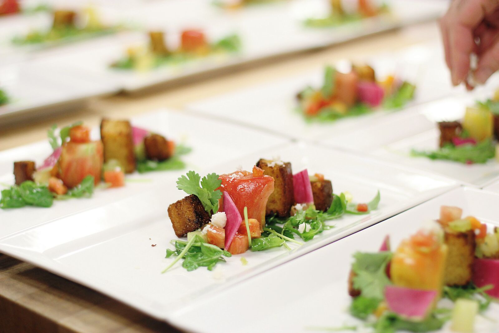A row of square plates with food arranged on them.
