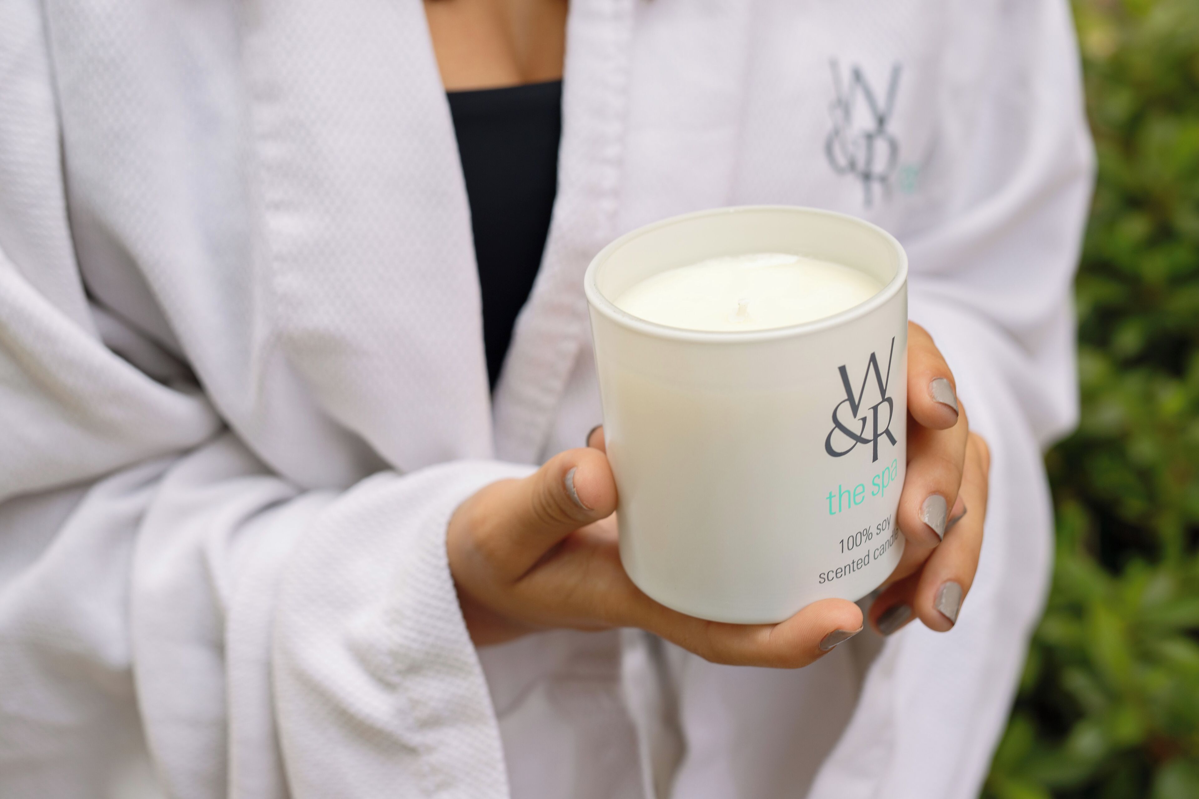 Una persona sosteniendo una vela blanca con el texto 'W&R the spa' y 'vela perfumada con aroma a soja 100 por ciento'.