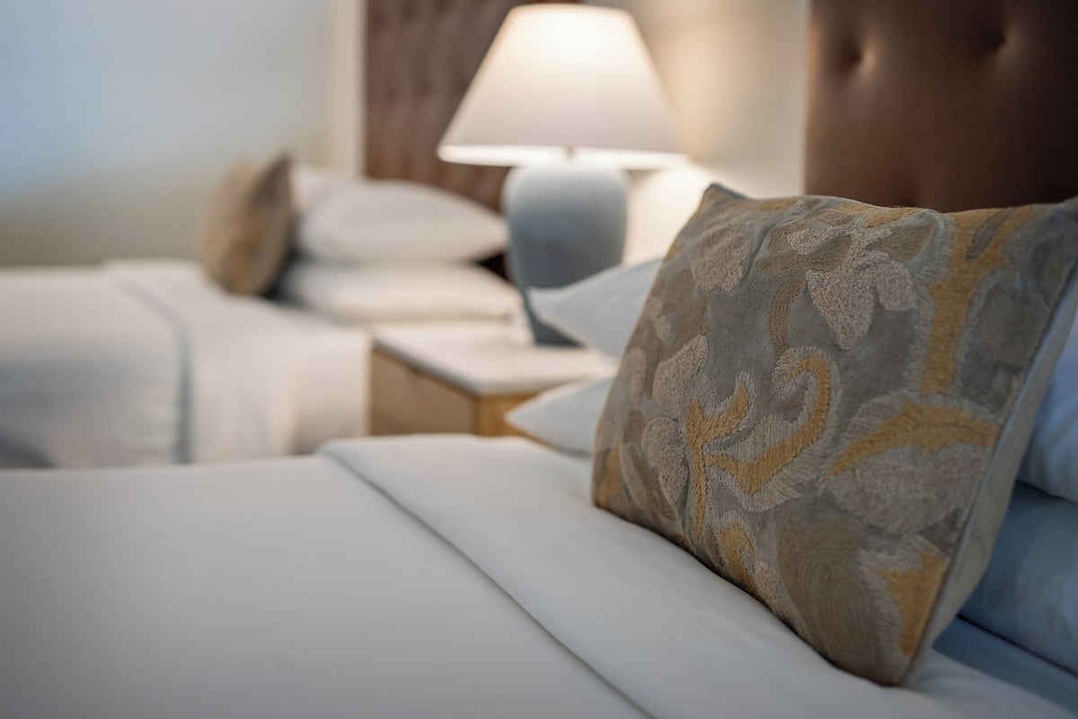 A hotel room with neatly made beds, a lamp on the nightstand, and a patterned pillow.