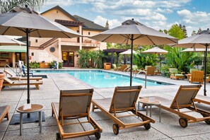 A poolside area with lounge chairs and umbrellas, a pool, and a building with a balcony.